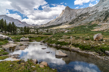 Fototapeta na wymiar View along the High Sierra Trail of Big Arroyo Creek and Mount Kaweah with a small lake and trees in the foreground under puffy clouds, Sequoia National Park, California