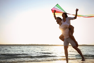 Happy couple playing with kite on beach near sea. Spending time in nature