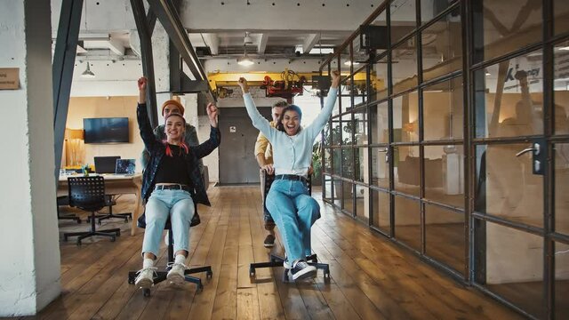 Office fun. Group of young casual coworkers competing in chair race in empty workspace