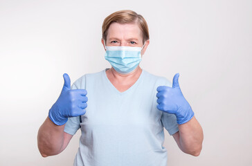 Elderly woman showing thumbs up while wearing mask and gloves