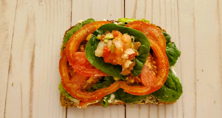A top view of avocado toast made with smashed avocado, yogurt, seasoning, sliced tomatoes, spinach leaves and fresh salsa