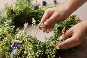 Woman making beautiful wreath of wildflowers at wooden table, closeup © New Africa