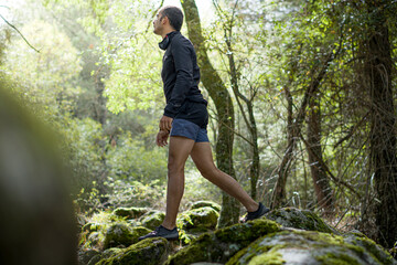 Hombre caminando por el bosque rodeado de musgo y piedras cerca de un río. Haciendo ejercicio en la naturaleza.