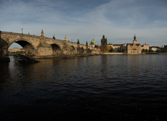 Fototapeta na wymiar the monument of Charles Bridge from 1402 and the level of the flowing Vltava river and the light from the sun at sunset in the center of Prague in the Czech Republic