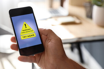 Man holding smartphone with warning about virus attack at home, closeup