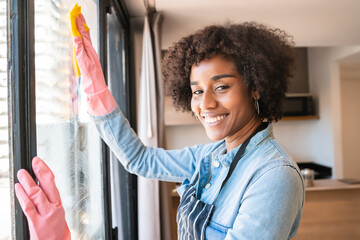 Afro woman cleaning window with rag at home. - obrazy, fototapety, plakaty