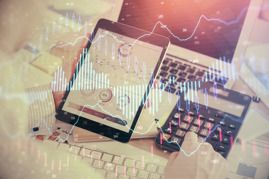 Double exposure of man's hands holding and using a digital device and forex graph drawing. Financial market concept.
