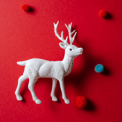 White reindeer toy with small balls of wool on red background.