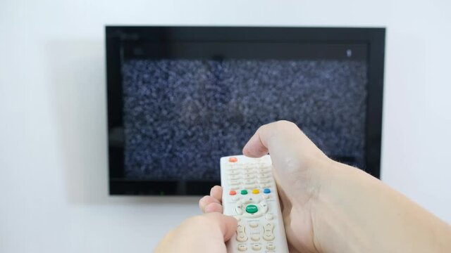 Hand with TV remote control in front of the screen with white noise on it - tuning the television channels and connecting problems
