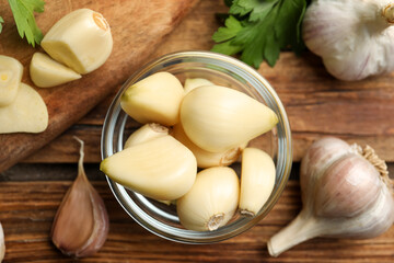Fresh peeled garlic cloves in bowl and bulbs on wooden table, flat lay. Organic product