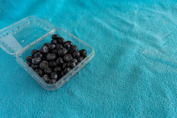 Fototapeta na wymiar fresh blueberries in plastic container on turquoise background