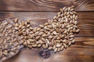 Plastic bag with pistachios on a wooden background. Nuts are scattered on the surface. Flat layout