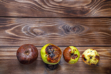 Rotten and moldy apples on a wooden background. Flat layout. Copy space
