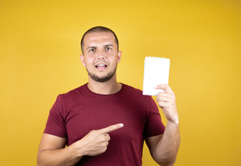 Russian man wearing basic red t-shirt over yellow insolated background smiling and showing blank notebook in her hand