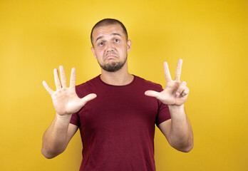 Russian man wearing basic red t-shirt over yellow insolated background showing and pointing up with fingers number eight while smiling confident and happy.