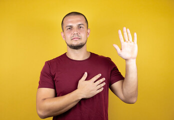 Russian man wearing basic red t-shirt over yellow insolated background smiling swearing with hand on chest and fingers up, making a loyalty promise oath