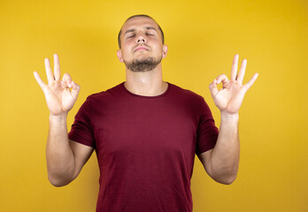 Russian man wearing basic red t-shirt over yellow insolated background relax and smiling with eyes closed doing meditation gesture with fingers. Yoga concept