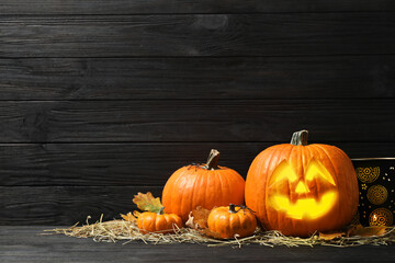 Jack o'lantern, pumpkins and straw on black wooden table, space for text. Halloween decor