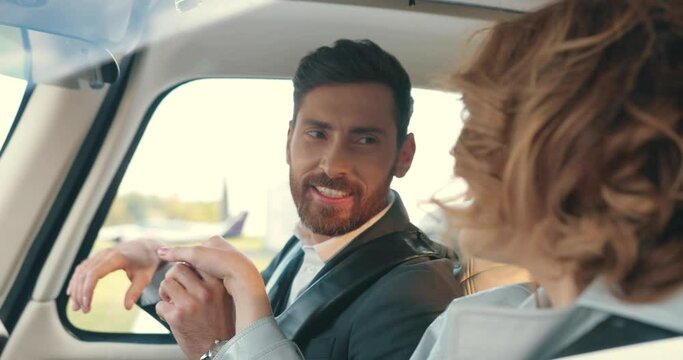 Close up portrait of happy Caucasian handsome bearded man speaking with beautiful young joyful woman while sitting in airplane on set. Male actor kisses female hand and talks. Film industry concept