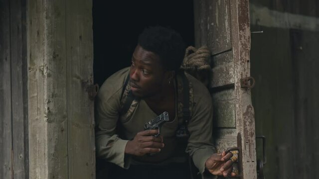 African man with gun leaving shack hiding from zombie in abandoned territory