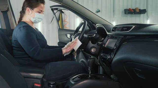 Woman in gloves and face mask cleans and disinfects car interior inside with antiseptic antibacterial disinfectant wipe, anti Covid-19, prevention of coronavirus.