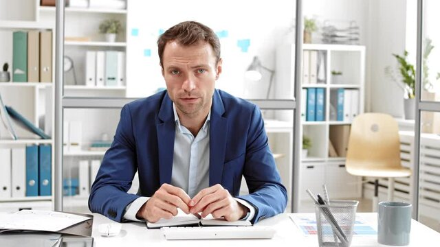 POV of middle-aged male Caucasian employee in blue blazer sitting by desk in spacious office, having online meeting with management, looking guilty and disappointed, nodding and putting head down