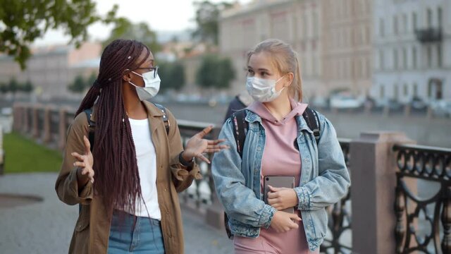 Multinational student women in medical mask talking walking down city street