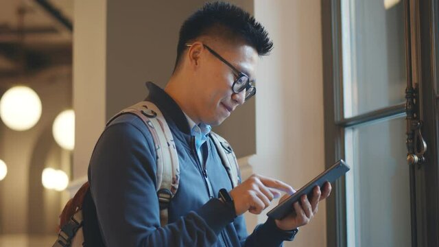 Smiling Male College Student Checking Mobile Phone In Campus Building