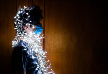 Young man with surgical mask, Christmas lights around. Christmas in times of coronavirus.