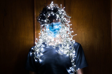 Young man with surgical mask, Christmas lights around. Christmas in times of coronavirus.