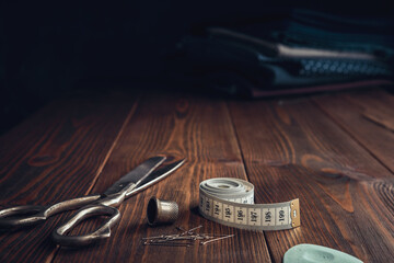 Sewing items - tailoring scissors, measuring tape, thimble, including pins. Stack of fabrics for sewing on background. Copy space for text.