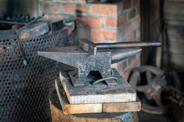 A vintage anvil and hammer on wood blocks in a forge or workshop. There's a steel hearth in the...