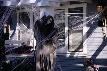 Death wearing a mask for coronavirus. Cobweb as decoration. Halloween scenery. Terrible holiday at home. Halloween in the USA. Traditions and house decor. Terrible creatures.
