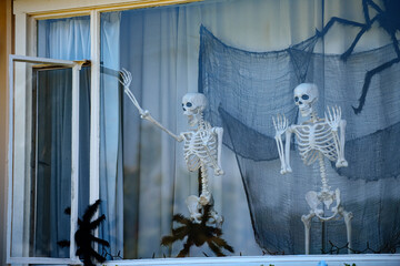 Skeletons waving from the window. Happy skeletons. Halloween scenery. Terrible holiday at home. Halloween in the USA. Traditions and house decor. Terrible creatures.