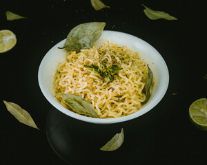 Sopa de fideos en plato blanco minimalista adornada con hojas sobre mesa negra