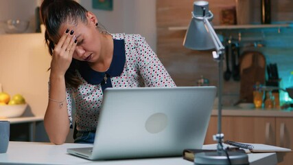 Stressed busy woman with headache working from home late at night on laptop. Tired focused employee using modern technology network wireless doing overtime for job reading writing, searching