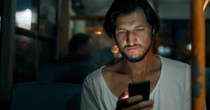 Happy young bearded man is using a smartphone app and smiling. Hipster is listening to music with headphones and texting a message