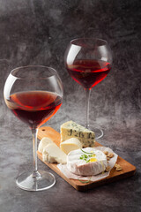 two glasses of red wine and different types of cheese.