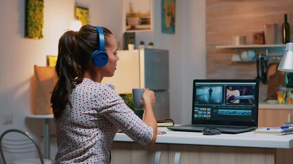 Woman video editor with headset working with footage and sound sitting in home kitchen. Woman videographer editing audio film montage on professional laptop sitting on desk in midnight