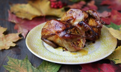 roasted quail stuffed with polenta with dried tomatoes, against the background of autumn leaves. autumn dish. game birds