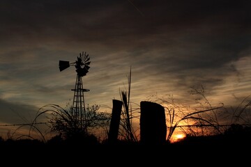Windmill silhouette at Sunset with a tree and clouds north of Hutchinson Kansas USA out in the country.