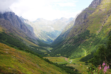 A green mountain valley, during which the river flows, and the tops of the rocks are covered with clouds and fog