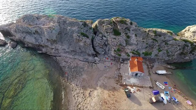 Aerial shot from drone of Mylokopi bay and beaches, Greece, with beautiful glimmering sea with tones of blue and turquoise, interesting rock formations, and with people who visited to camp and to swim