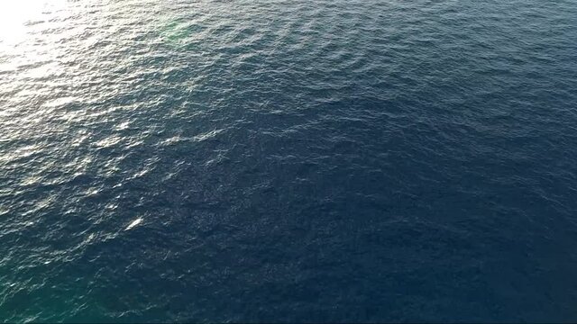 Low-flying aerial shot from drone of Mylokopi bay, Greece, with beautiful glimmering and shining sea with tones of blue and turquoise