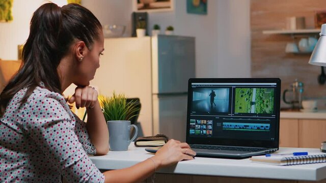 Videographer editing from home on professional laptop sitting on desk in modern kitchen in midnight. Creative video editor working at night at new project processing audio film montage.