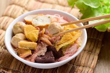 Thai food (Yen Ta Fo), Rice noodles soup with red sauce and fish tofu, pork ball and fried wonton in a bowl eating by chopsticks