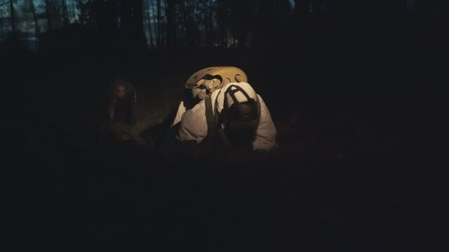 Zombie chasing human in protective overall in dark forest