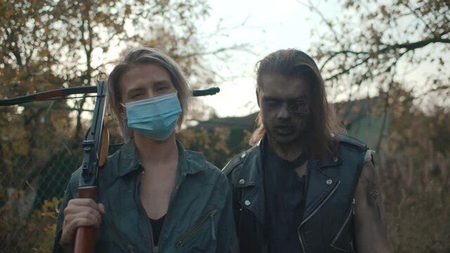 Portrait of woman warrior with crossbow and male zombie outdoors