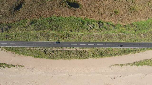 Birds eye view of car driving along scenic highway by sandy beach