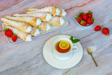 Puff pastry rolls with protein cream on a white plate, near strawberries and tea